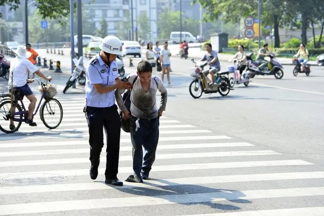 A beggar who lay at the side of a road pretending he had no legs was moved on by police who made him stand up and walk away. The man lay slumped on his front in Chengdu, in Sichuan Province, China, with his legs tucked under him, and his jeans stretched out to make it appear he had no legs. He is approached by a police officer, who bends down and talks to him for some moments. (Photo by Rex Features)