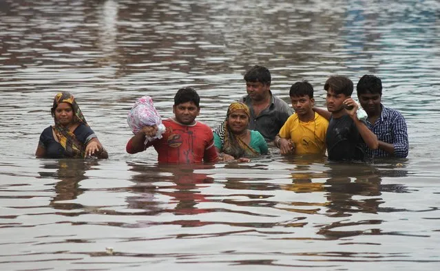 Indians wade through a waterlogged street in Ahmadabad, India, Wednesday, July 30, 2014. Normal life was thrown out of gear and rail and air traffic in several areas of Gujarat state were disrupted due to heavy rainfall, according to news reports. (Photo by Ajit Solanki/AP Photo)