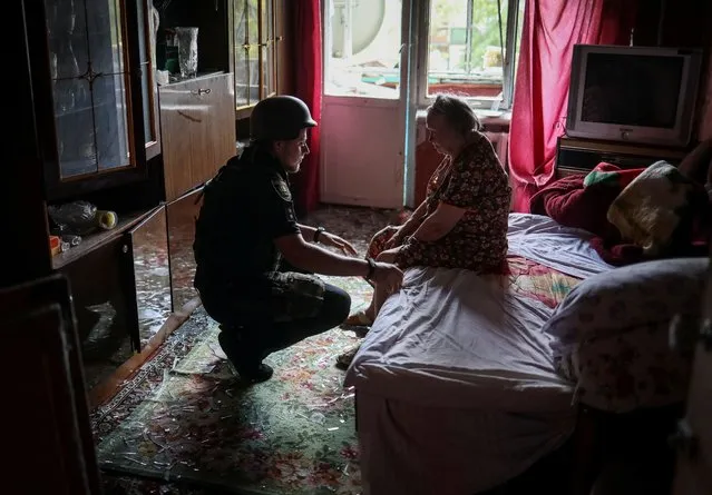 A police officer helps an elderly woman leave her flat in a residential building damaged by a Russian military strike, amid Russia's invasion on Ukraine, in Kramatorsk, in Donetsk region, Ukraine on July 19, 2022. (Photo by Gleb Garanich/Reuters)