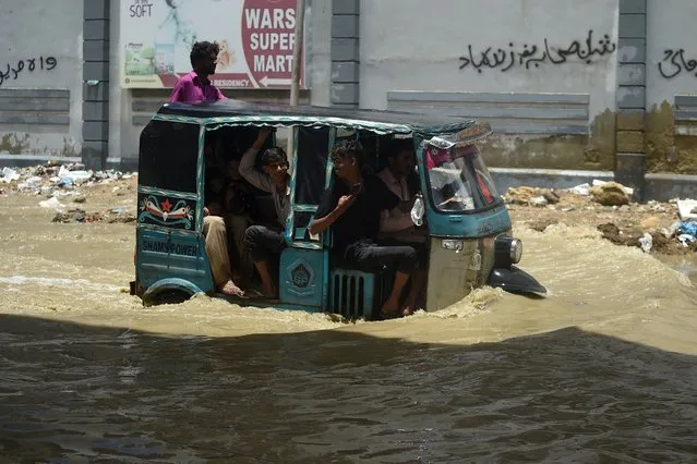 Commuters travel in a vehicle through a waterlogged road after a heavy rain shower in Karachi on July 11, 2022. (Photo by Rizwan Tabassum/AFP Photo)