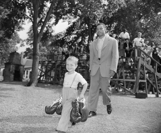 Joe Louis gets a helping hand from 4 year old Butch Hopper who carries his gloves from the ring at Louis training camp, at Pompton lakes, N.J., June 21, 1948 after the heavyweight champ finished training. (Photo by Harry Harris/AP Photo)