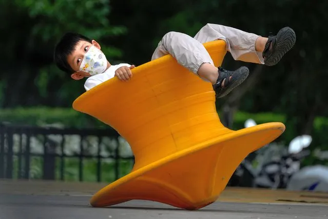 A kid wearing a face mask plays on a balancing chair at a green space in Beijing, Monday, August 8, 2022. (Photo by Andy Wong/AP Photo)