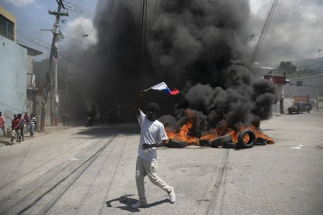 A man waving a Russian national flag as he hopes for support from the Russian government, walks past a burning barricade set up by protesters demanding that Haitian Prime Minister Ariel Henry step down and a call for a better quality of life, in Port-au-Prince, Haiti, Wednesday, September 7, 2022. (Photo by Odelyn Joseph/AP Photo)