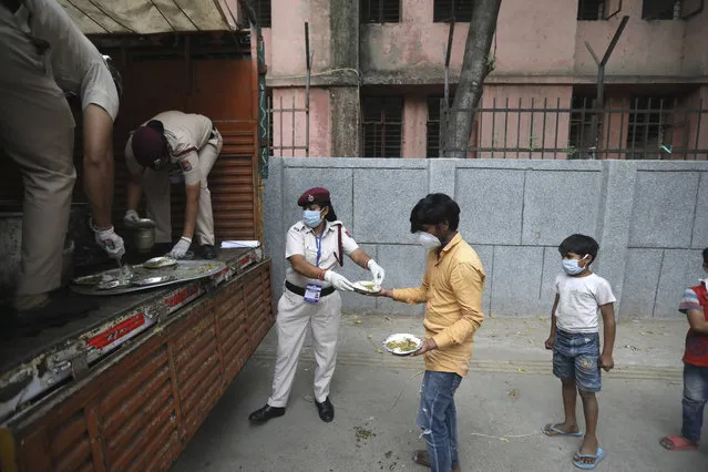 Delhi policewomen distribute food prepared by the Bangla Sahib Gurudwara kitchen in an impoverished locality in New Delhi, India, Sunday, May 10, 2020. The Bangla Sahib Gurudwara has remained open through wars and plagues, serving thousands of people simple vegetarian food. During India's ongoing coronavirus lockdown about four dozen men have kept the temple's kitchen open, cooking up to 100,000 meals a day that the New Delhi government distributes at shelters and drop-off points throughout the city. (Photo by Manish Swarup/AP Photo)