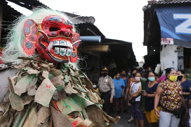 A police officer wearing a Balinese traditional mask, called celuluk, performs as the new coronavirus during a campaign to wear masks as a precaution against the virus outbreak at a market in Bali, Indonesia, Thursday, May 14, 2020. (Photo by Firdia Lisnawati/AP Photo)