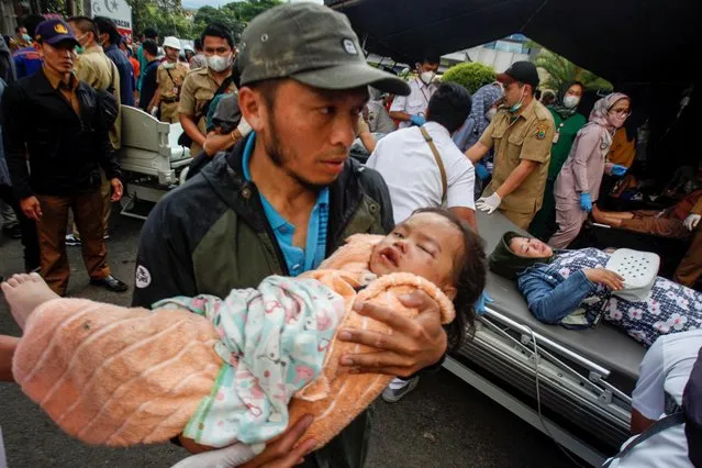 A man carries an injured child to receive treatment at a hospital, after an earthquake hit in Cianjur, West Java province, Indonesia on November 21, 2022. (Photo by Yulius Satria Wijaya/Antara Foto)