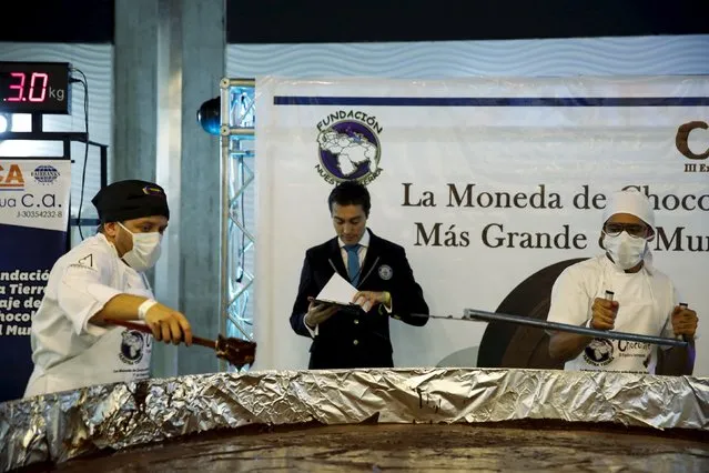 Carlos Martinez (L), a representative of the Guinness World Records, examines the cooking process of a chocolate coin during an attempt to break the Guinness World Record for the biggest chocolate coin in Caracas, Venezuela, October 1, 2015. (Photo by Carlos Garcia Rawlins/Reuters)