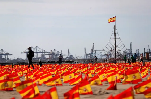 People walk along La Patacona beach that is carpeted with a total of 53,000 Spanish flags to pay a tribute to the fatalities caused by the COVID-19 virus disease, in the town of Alboraya, eastern Spain, 04 October 2020. The flags were placed in the early morning by volunteers from the National Association for Coronavirus Victims initiative. (Photo by Manuel Burque/EPA/EFE)