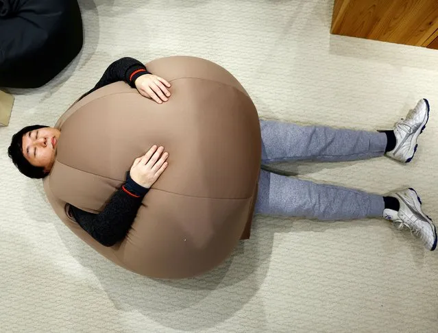 Customer Ryuji Baba poses while he tries on the wearable beanbag during a photo opportunity at a pop-up booth of the Shinjuku Marui main department store in Tokyo, Japan on February 6, 2023. While the beanbag's onion-shaped goofy style made it a hit on Japanese social media earlier this month, the main goal was relaxation, according to Shogo Takikawa, a representative of the beanbag's manufacturer, Takikou Sewing. (Photo by Kim Kyung-Hoon/Reuters)