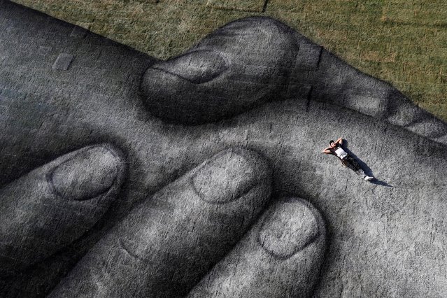 French-Swiss street artist Saype poses as he works on his artwork on a floating barge over the Golden Horn in Istanbul, Turkey on October 23, 2020, as part of the “Beyond Walls” project to create a spray-painted “human chain” across the world to encourage humanity and equality. (Photo by Murad Sezer/Reuters)