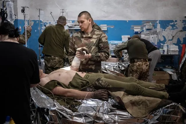 Medics treat wounded Ukrainian soldiers inside a frontline medical stabilisation point, amid Russia's attack on Ukraine, near Vuhledar, Donetsk region, Ukraine on February 19, 2023. Viktor's team of seven medics and six nurses toils away, hemmed in by racks of medical supplies and portable heaters. (Photo by Marko Djurica/Reuters)