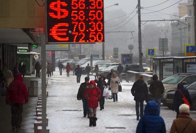 People walk past a sign advertising currency exchange rates in Moscow, Russia, Friday, December 12, 2014. The ruble hit another record low against the dollar even after Russia's Central Bank sought to ease the selling pressure on the currency by raising interest rates again. (Photo by Alexander Zemlianichenko/AP Photo)