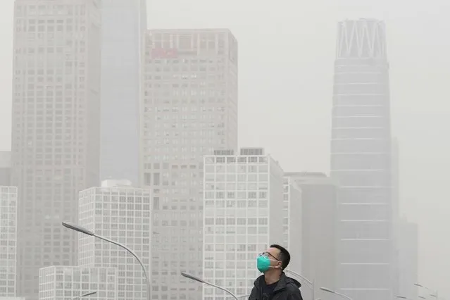 A man wearing a face mask walks on an overhead bridge against the office buildings in the central business district as dust and sand storm sweeps through Beijing, Thursday, April 13, 2023. Many areas in northern China were blanketed with floating sand and dust on Thursday, and a sandstorm was expected to sweep through parts of Inner Mongolia. (Photo by Andy Wong/AP Photo)