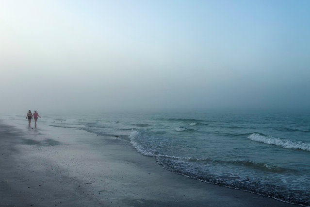 People walk along the beach at the barrier island of Lido Key during early morning fog in Sarasota, Florida, U.S. November 9, 2025. (Photo by Shannon Stapleton/Reuters)