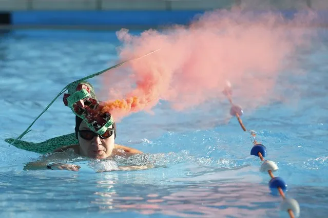 A swimmer competes with a smoking flare and a paper mache dragon on his head during the UK Cold Water Swimming Championships at Tooting Bec Lido in south London January 24, 2015. (Photo by Luke MacGregor/Reuters)