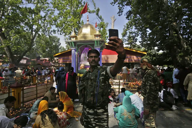 An Indian paramilitary soldier takes a selfie as Kashmiri Hindu devotees known as “pandits” offer prayers during the annual festival at the Kheer Bhawani temple in Tul Mul, outskirts of Srinagar, India, Wednesday, June 20, 2018. (Photo by Mukhtar Khan/AP Photo)