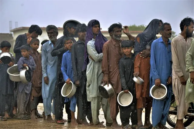 People wait their turn to get free food distributed by volunteers during rain outside a camp of internally displaced people from coastal areas due to Cyclone Biparjoy approaching, in Sujawal, Pakistan's southern district in the Sindh province, Thursday, June 15, 2023. A vast swath of western India and neighboring southern Pakistan that suffered deadly floods last year are bracing for a new deluge as fast-approaching Cyclone Biparjoy whirls toward landfall Thursday. (Photo by Pervez Masih/AP Photo)