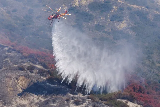 A helicopter drops water as it assists firefighters battling a hillside fire that burned through a neighborhood and destroyed homes in Laguna Niguel, California, U.S., May 12, 2022. (Photo by Mike Blake/Reuters)