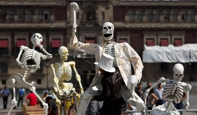 A man carries an artwork of a skeleton in preparation for the Day of the Dead celebrations in Mexico City's Zocalo, Tuesday, October 29, 2013.  Mexicans celebrate Day of the Dead to honor deceased loved ones, a tradition that coincides with All Saints Day and All Souls Day on November 1 and 2. (Photo by Eduardo Verdugo/AP Photo)