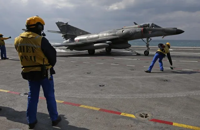 A “Yellow dog” flight deck director gives the go signal to a Super Etendard fighter jet as his chief looks on on France's Charles de Gaulle aircraft carrier on mission in the Gulf, January 29, 2016. (Photo by Philippe Wojazer/Reuters)