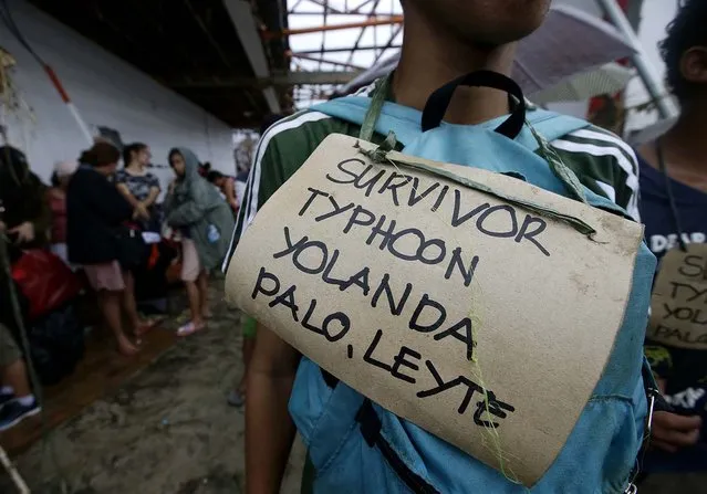 Typhoon survivors hang signs from their necks as they queue up in the hopes of boarding a C-130 military transport plane Tuesday in Tacloban. (Photo by Bullit Marquez/Associated Press)