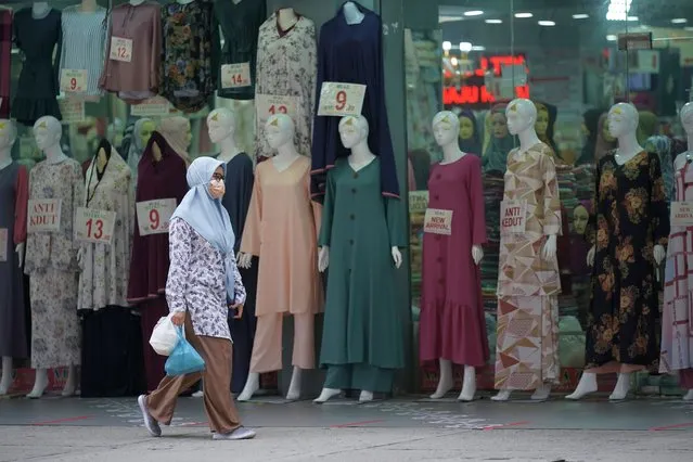In this Friday, April 19, 2021, photo, a woman wearing a protective mask passes a clothing shop in the Ramadan bazaar in Kuala Lumpur, Malaysia. Malaysian Prime Minister Muhyiddin Yassin announced Monday that the whole country will be placed under a near lockdown for about a month but all economic sectors will be allowed to operate. (Photo by Vincent Thian/AP Photo)