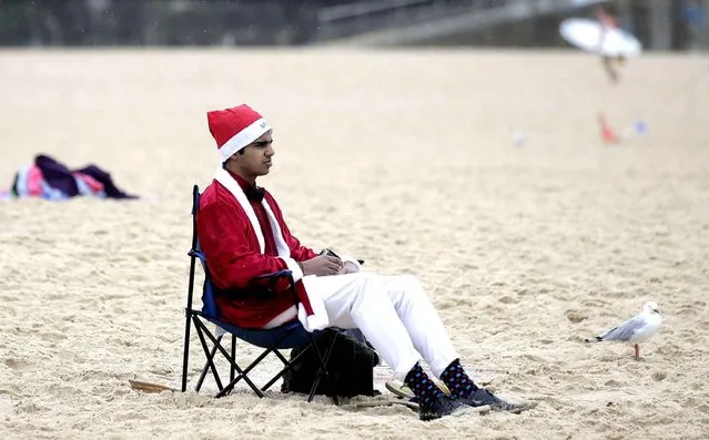 Kabir Singh, who is from the U.S. but now lives in Australia, sits on Bondi Beach wearing a Santa suit as light rain falls on him while celebrating Christmas Day in Sydney, Wednesday, December 25, 2013. (Photo by Rick Rycroft/AP Photo)