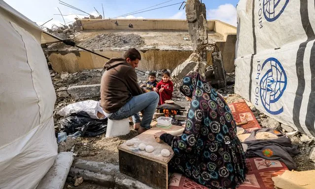 A woman prepares fresh dough for bread as she sits next to a man and children outside tents by the rubble of a destroyed building in Rafah in the southern Gaza Strip on January 2, 2024, amid the ongoing conflict between Israel and the Palestinian militant group Hamas. (Photo by AFP Photo/Stringer)