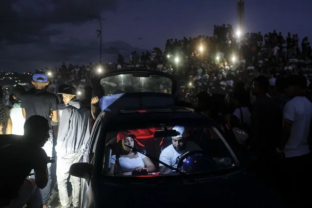 A couple turns on the music in their car during a motorcycle stunt exhibition in the Petare neighborhood of Caracas, Venezuela, Sunday, September 26, 2021. (Photo by Matias Delacroix/AP Photo)