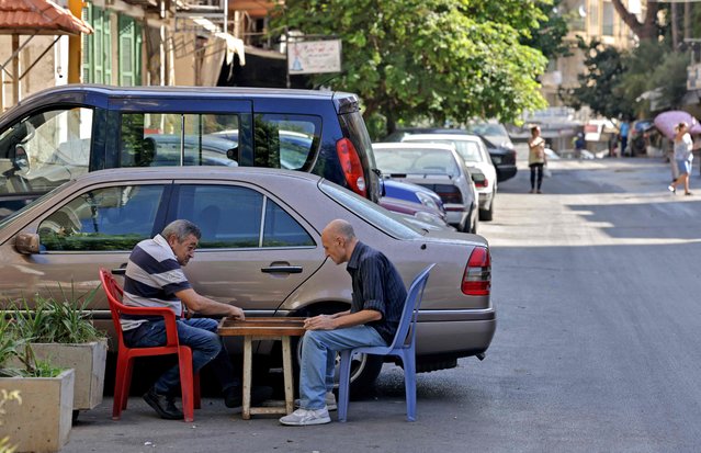 Lebanese men play backgammon in the Christian neighbourhood of Ain al-Remmaneh, adjacent to the area of Tayouneh, in the southern suburb of the capital Beirut on October 15, 2021, a day after deadly clashes. Lebanon prepared to bury the victims of its deadliest sectarian unrest in years a day after gunfire gripped central Beirut for hours and revived the ghosts of the civil war. (Photo by Joseph Eid/AFP Photo)