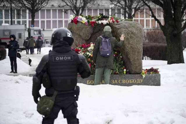 A police officer watches as a man lays flowers paying the last respect to Alexei Navalny at the monument, a large boulder from the Solovetsky islands, where the first camp of the Gulag political prison system was established, in St. Petersburg, Russia on Saturday, ebruary 17, 2024. (Photo by Dmitri Lovetsky/AP Photo)
