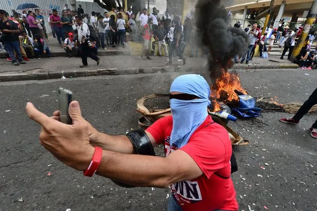 A student makes a selfie next to a bonfire during a protest against Honduran President Juan Orlando Hernandez in the surroundings of the Congress building in Tegucigalpa, on May 22, 2019. The students demand the Congress to derogate at leat 11 decrees regarding health and education. (Photo by Orlando Sierra/AFP Photo)