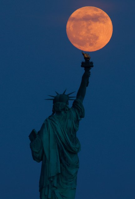 The full Flower Moon rises behind the Statue of Liberty at twilight in New York City on May 22, 2024, as seen from Jersey City, New Jersey. (Photo by Gary Hershorn/Getty Images)
