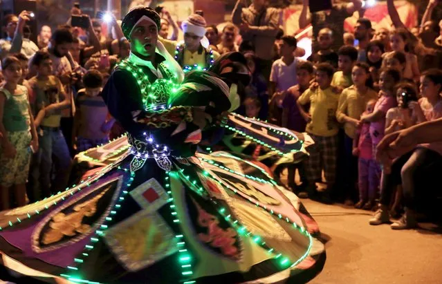 Children watch as a whirling dervish performs a traditional (Al-Tannoura Egyptian folk dance) Sufi dance during the Muslim fasting month of Ramadan at a celebration in front of a historical mosque of Sultan al-Ashraf Qaitbey, and near a Sufi concert in the old Islamic area of Cairo, Egypt, July 8, 2015. (Photo by Amr Abdallah Dalsh/Reuters)