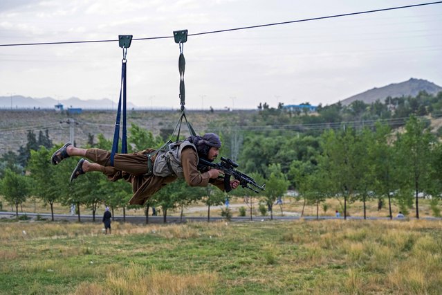 A Taliban security personnel holds his gun as he rides zipline near the Qargha lake on the outskirts of Kabul on July 4, 2024. (Photo by Wakil Kohsar/AFP Photo)