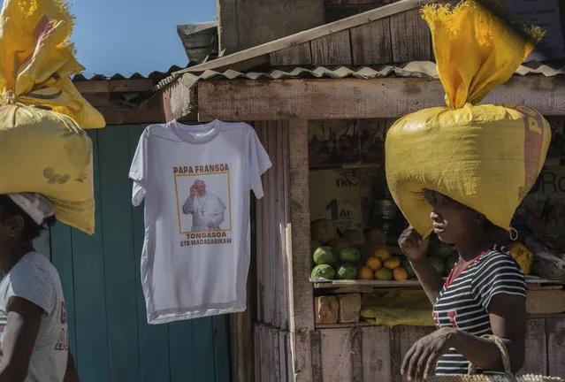 Women carrying bags on their heads pass a stall selling Pope t-shirts ahead of the Popes visit to Madagascar next weekend, in Antananarivo, Madagascar, Friday, August 30, 2019. Pope Francis' will visit the three nations of Mozambique, Madagascar, and Mauritius, Sept. 4-10. (Photo by Alexander Joe/AP Photo)