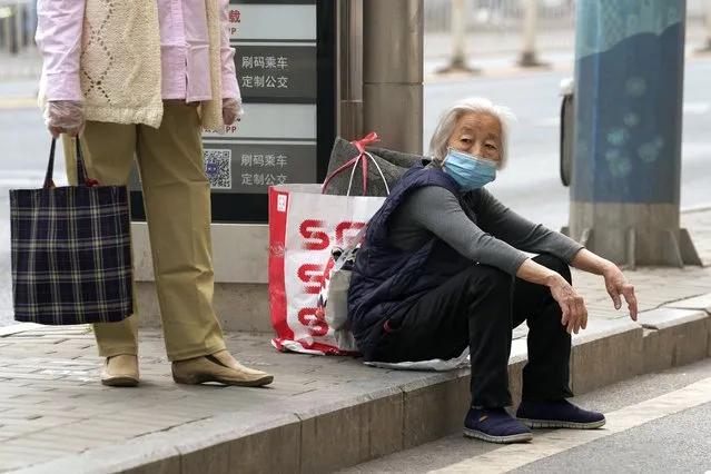 An elderly woman wearing mask waits at a bus-stop in Chaoyang District on Monday, April 25, 2022, in Beijing. (Photo by Ng Han Guan/AP Photo)