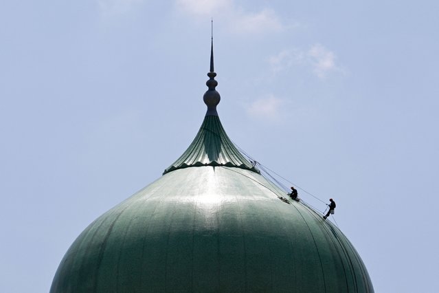 Two workers work on the main dome of the Malaysian Prime Minister's Office in Putrajaya on June 4, 2024. (Photo by Mohd Rasfan/AFP Photo)