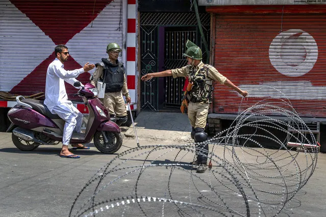 Indian paramilitary soldiers question a person on a scooter before letting him pass at a barbed-wire road checkpoint set up by Indian security forces in Srinagar, Indian controlled Kashmir, Friday, July 7, 2017. Government forces imposed curfew-like restrictions in many parts of Indian controlled Kashmir to stop anti Indian protests ahead of the first death anniversary of rebel leader Burhan Wani on Saturday. His killing by security forces last year sparked violent street clashes and almost daily protests throughout the region. (Photo by Dar Yasin/AP Photo)
