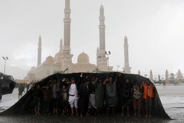 People cover themselves as protesters, mainly Houthi supporters, gather for a rally to show solidarity with Palestinians in the Gaza Strip, during heavy rains, in Sanaa, Yemen on August 23, 2024. (Photo by Khaled Abdullah/Reuters)