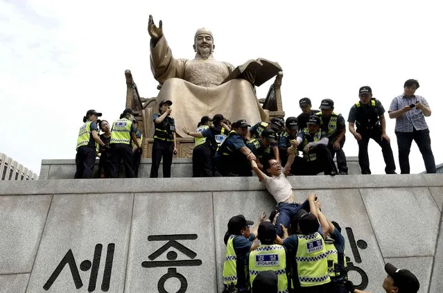 A member from a part-time workers organization is detained by police officers as he stages a rally demanding an increase in the minimum wage to 10,000 won (US$8.71) per hour from the current 6,030 won (US$5.25) on the statue of King Sejong in Seoul, South Korea, Tuesday, July 12, 2016. Laborers are calling for the increase of the minimum wage for next year while employers insist on a freeze, according to Yonhap news agency. (Photo by Ahn Young-joon/AP Photo)