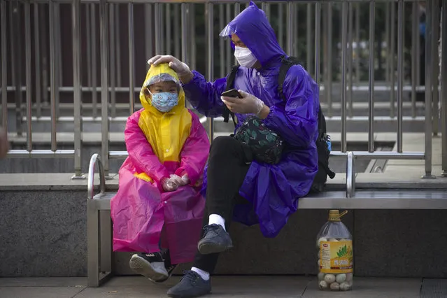 Passengers wearing face masks and raincoats to protect against the spread of new coronavirus sit outside of Hankou train station after of the resumption of train services in Wuhan in central China's Hubei Province, Wednesday, April 8, 2020. (Photo by Ng Han Guan/AP Photo)