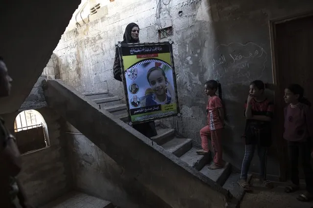 A relative of 11-year-old Layan al-Shaer holds a poster showing her photo, during her funeral in Khan Younis, in the Gaza Strip, Thursday, August 11, 2022. On Thursday, Layan died of her wounds after she was injured in last week's Israeli air strikes. (Photo by Fatima Shbair/AP Photo)
