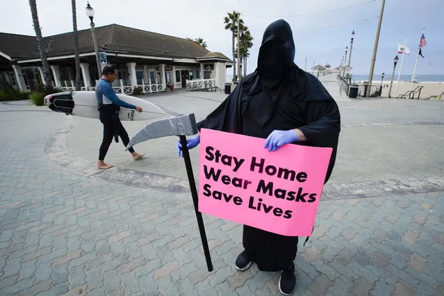 Spencer Kelly, dressed as the grim reaper, demonstrates in favor of the stay-at-home order during the coronavirus pandemic at the pier Friday, May 8, 2020, in Huntington Beach, Calif. (Photo by Chris Carlson/AP Photo)