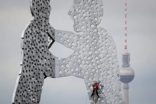 An industrial climber salvages a children's bicycle from the aluminium sculpture “Molecule Man” by US artist Jonathan Borofsky on the river Spree in Berlin, Germany, 23 August 2015. The salvage operation on the 30-metre-high artwork took around one and a half hours. The climbing experts climbed up on the holes of the artwork with a rope and sawed off the bicycle. Why and how it came to be there is still a mystey. (Photo by Kay Nietfeld/EPA)