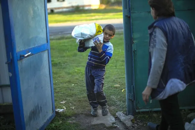 A young boy carries a bag with food given by Ukrainian volunteers in recently retaken Pidlyman village, east Ukraine, Friday, October 7, 2022. (Photo by Francisco Seco/AP Photo)