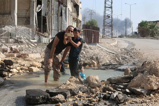 A man and a boy inspect a mobile phone as they cool down with water from a damaged water pipe due to shelling in the rebel held neighbourhood of Sheikh Saeed, in Aleppo, Syria  August 20, 2016. (Photo by Abdalrhman Ismail/Reuters)