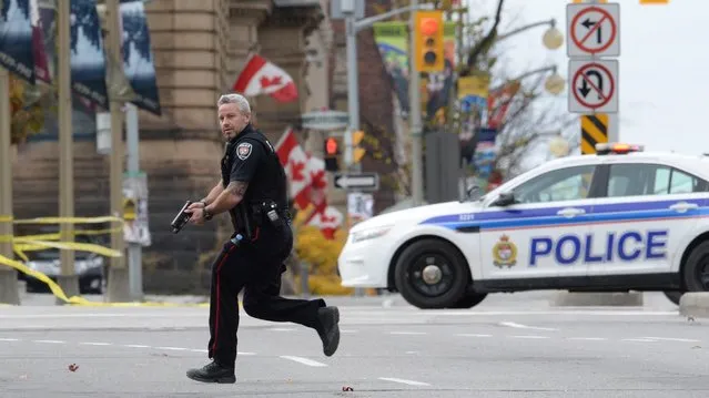 An Ottawa police officer runs with his weapon drawn outside Parliament Hill in Ottawa on Wednesday October 22, 2014. (Photo by Sean Kilpatrick/AP Photo/The Canadian Press)