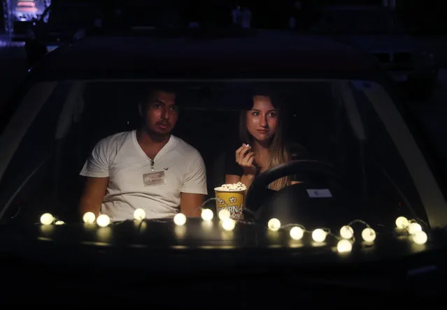 A couple sit on their car watch "Hours" at a drive-in movie event at a park, in Byblos town, north of Beirut, Lebanon, Friday, July 17, 2020. A group of Lebanese fresh university graduates have launched a drive-in cinema, bringing back the experience that has recently been making a comeback worldwide, as movie theaters remain close because of the coronavirus pandemic. The drive-in cinema experience in Lebanon comes with a special twist, with all proceeds going to needy families to help deal with the country's economic crisis. (Photo by Hussein Malla/AP Photo)