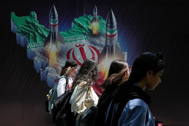 Iranian women without wearing their mandatory Islamic headscarf walk past a banner showing missiles being launched from Iranian map in northern Tehran, Iran, Friday, April 19, 2024. Iran fired air defenses at a major air base and a nuclear site near the central city of Isfahan after spotting drones early Friday morning, raising fears of a possible Israeli strike in retaliation for Tehran's unprecedented drone-and-missile assault on the country. (Photo by Vahid Salemi/AP Photo)